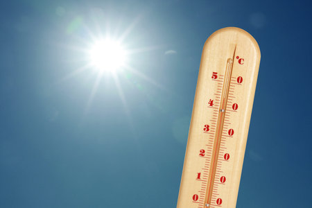 Thermometer showing high temperature against sky with bright sun. Extremely hot weather