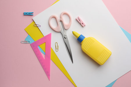 Glue in bottle, color paper and other stationery on pink background, flat lay