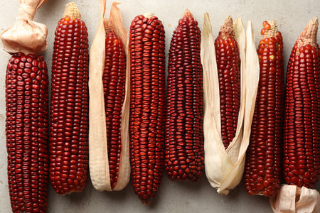 Ripe red corn cobs on light table against, flat lay