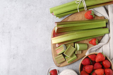 Fresh rhubarb stalks and strawberries on light table, flat lay. Space for textの写真素材