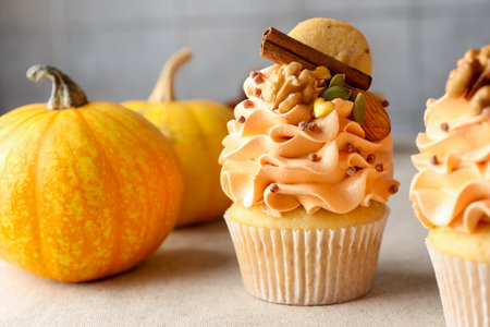 Delicious cupcakes with color cream, spices, cookies, nuts and autumn decor on gray table, closeup