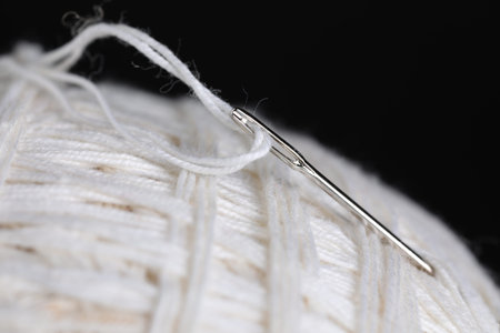 Sewing needle with white thread on black background, macro view