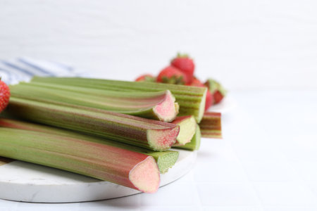Fresh rhubarb stalks and strawberries on white table, closeup. Space for text