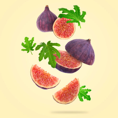 Fresh sweet figs and green leaves falling against beige background