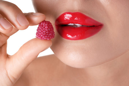 Woman with red lipstick on her lips and raspberry candy against white background, closeup