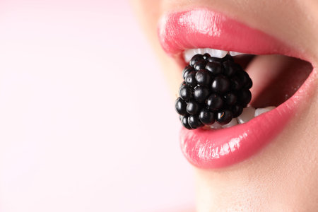 Woman with lipstick on her lips and blackberry against pink background, macro view. Space for textの写真素材