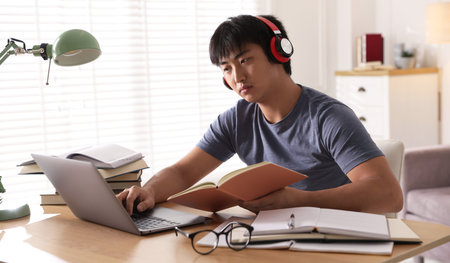 Student in headphones with laptop and books preparing for exam at table indoorsの写真素材
