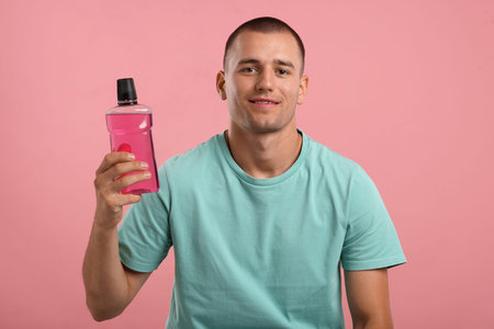 Man with bottle of mouthwash on pink background