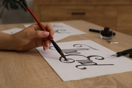 Calligraphy. Woman with brush writing words The End on sheet of paper at wooden table, closeupの写真素材