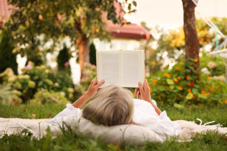 Senior woman reading book on blanket in gardenの写真素材