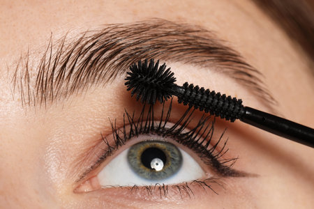 Woman applying mascara onto her eyelashes, closeup