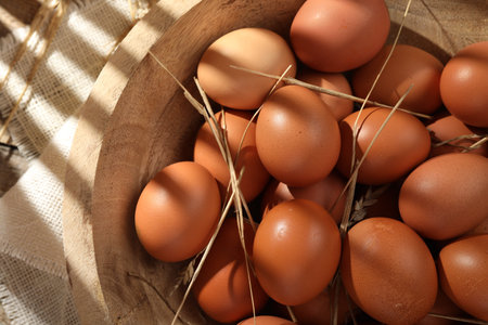 Raw chicken eggs and straw in bowl on table, top view