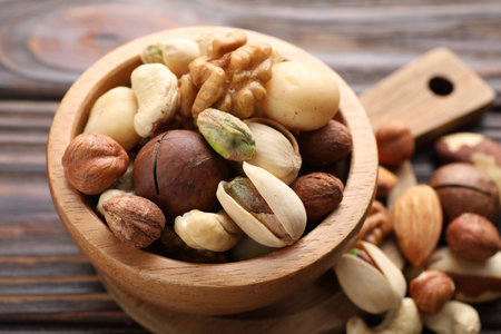 Mix of different nuts in bowl on wooden table, closeup
