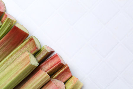 Fresh rhubarb stalks on white tiled table, flat lay. Space for textの写真素材