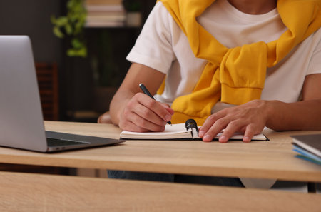 Man taking notes while passing online test via laptop at table indoors, closeup