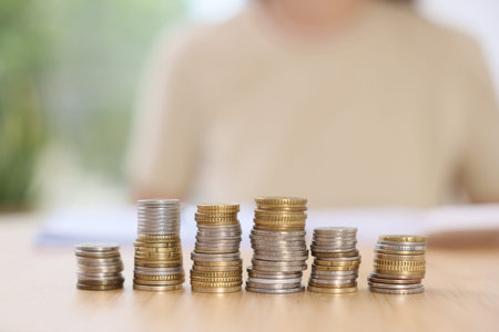 Woman at wooden table indoors, focus on stacks of coins