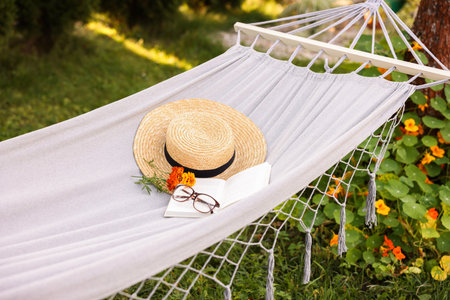 Straw hat, glasses, book and flowers on hammock outdoorsの写真素材