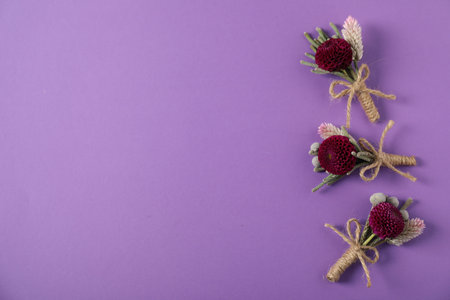 Stylish boutonnieres with flowers on purple background, flat lay. Space for text