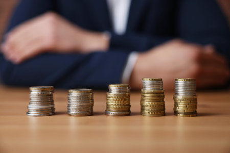 Man at wooden table indoors, focus on stacks of coins
