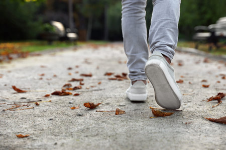 Man in stylish sneakers walking on asphalt outdoors, closeup.