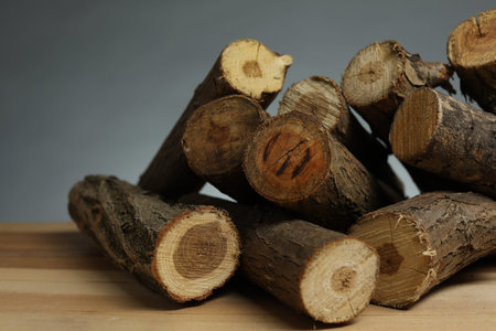 Pile of cut firewood on wooden table against gray background, closeup