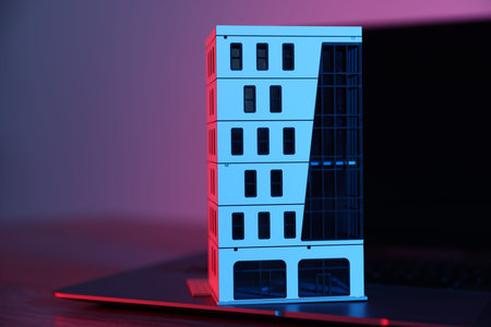 Real estate. Apartment building model and laptop on table in neon lights, closeup. Space for text