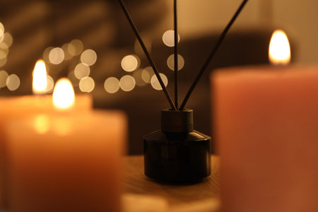 Burning candles and reed air freshener on table against blurred lights, closeup