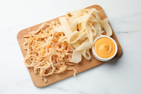 Dried shredded squid, shavings and sauce on white marble table, top view