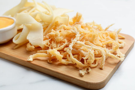 Dried shredded squid, shavings and sauce on white marble table, closeup