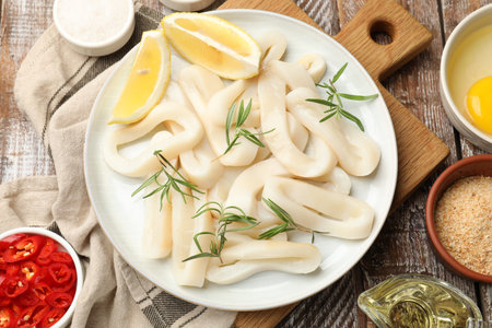 Uncooked squid rings, spices, yolk and bread crumbs on wooden table, flat lay