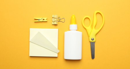Glue and other stationery on yellow background, flat lay