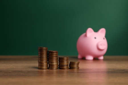 Coins and piggy bank on wooden table against green background, selective focus. Space for text