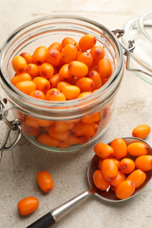 Fresh sea buckthorn berries in glass jar on beige table, closeup