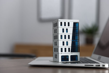 Real estate. Apartment building model and laptop on table indoors, closeup