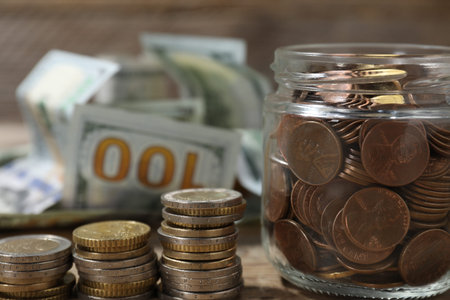 Glass jar with coins and banknotes on wooden table, closeup
