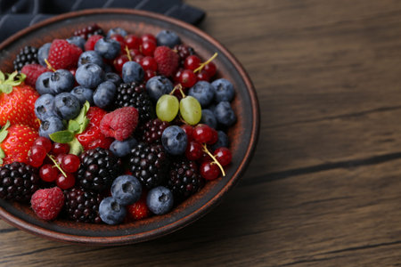 Different ripe berries in bowl on wooden table, closeup. Space for textの写真素材