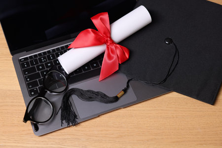 Graduation cap, diploma, laptop and glasses on wooden table, above view