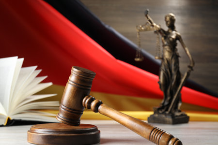 Judge's gavel, book and statue of Lady Justice on wooden table against flag of Germany, closeupの写真素材