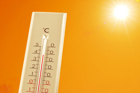 Thermometer showing high temperature against orange sky with bright sun. Extremely hot weather