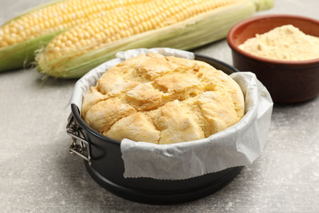 Freshly baked cornbread in cake pan on gray textured table, closeup