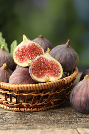 Fresh ripe figs in wicker basket on wooden table outdoors, closeup