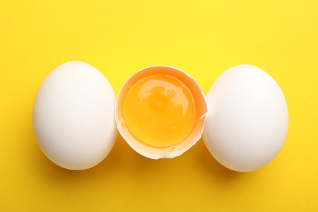 Whole and broken chicken eggs on yellow background, flat lay