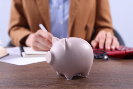 Piggy bank on wooden table and woman working indoors, selective focusの写真素材