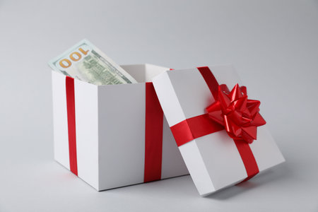 Gift box with dollar banknotes on light gray background