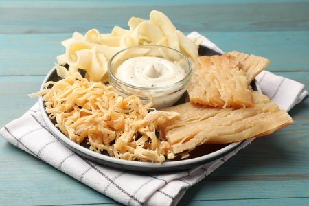 Dried squid and sauce on light blue wooden table, closeup