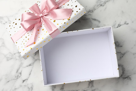 Opened gift box with beautiful lid on white marble table, top view