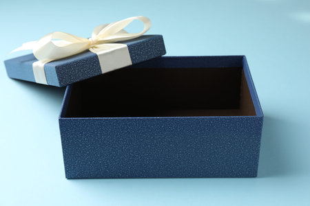 Opened gift box with beautiful lid on light blue background, closeup