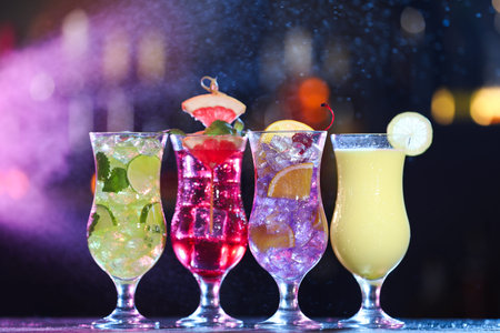 Glasses of alcoholic cocktails with garnish on table against blurred background with smoke