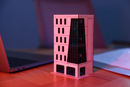 Real estate. Apartment building model and laptop on table in neon lights, closeup