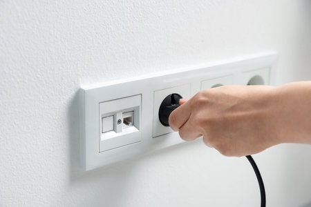 Woman putting plug into power socket on white wall, closeup